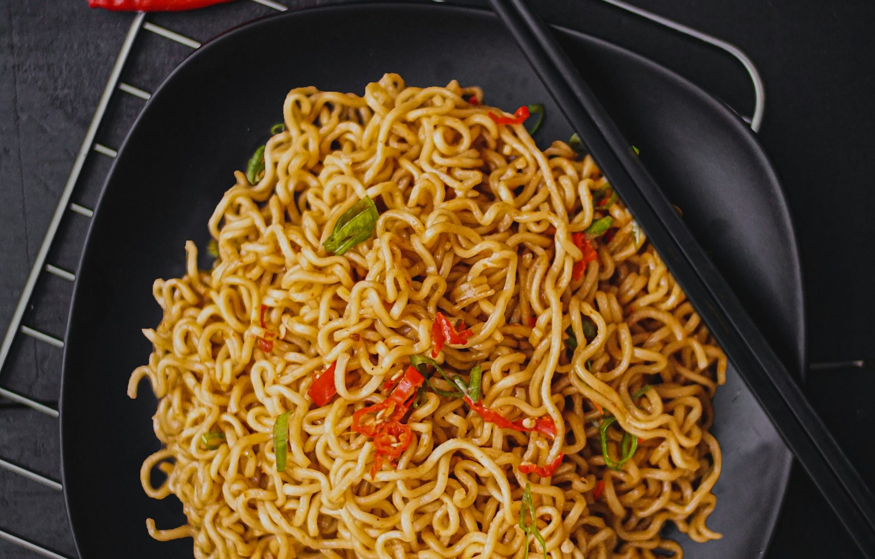 Close-up of stir-fried noodles with chilli and spring onion on a dark plate